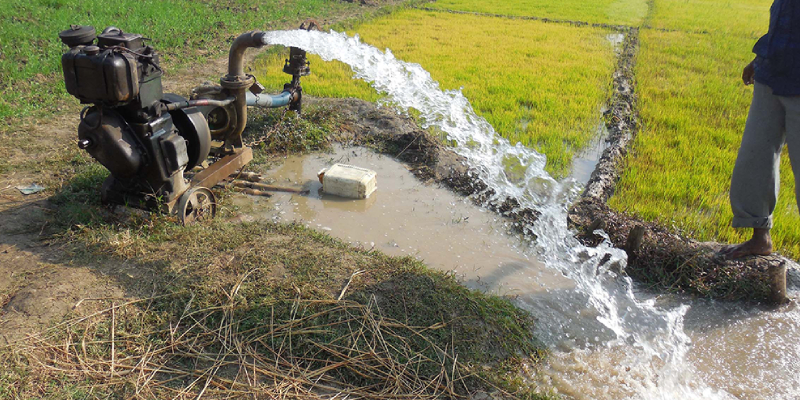 A man standing near the pump releasing water in the field